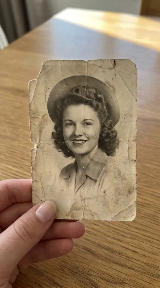 Before restoration: a creased, faded black-and-white portrait of a young woman, held in a hand