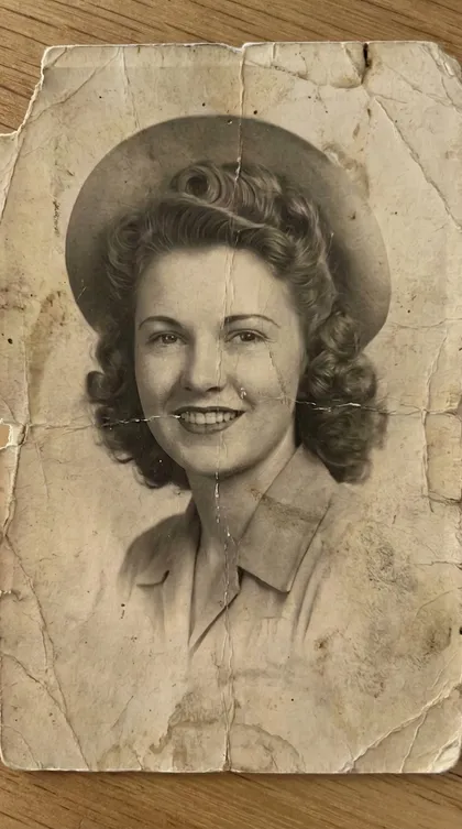 Old black-and-white portrait of a young woman in a hat, covered in creases, tears, and stains